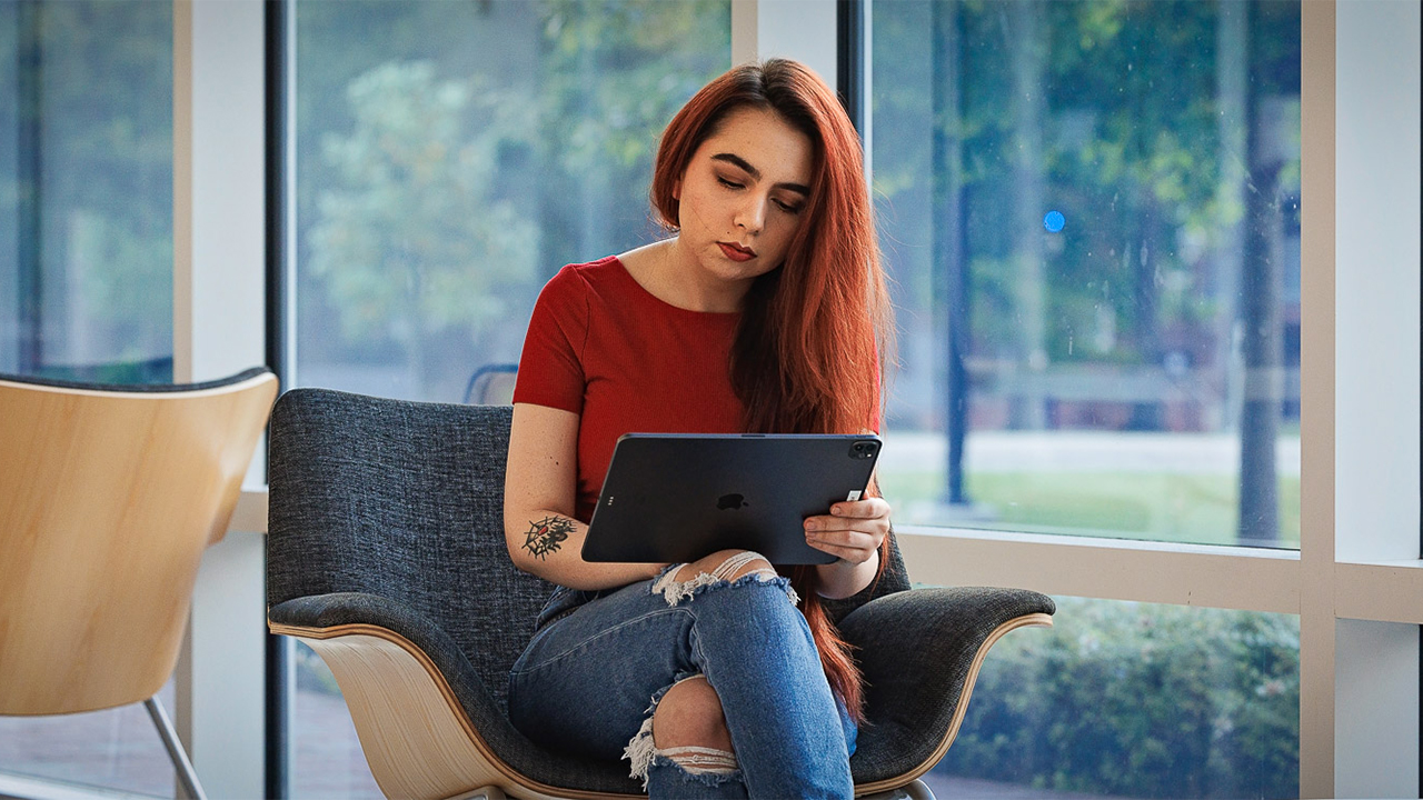A student sits on a chair and looks at a tablet computer.