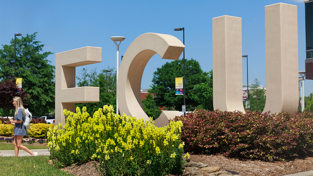 A student walks by the large concrete ECU letters.